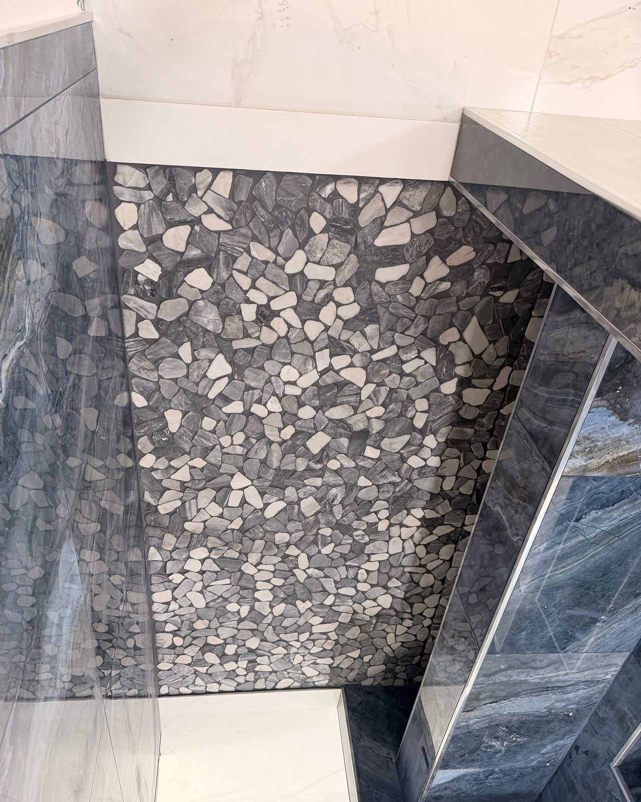 Shower corner with pebble accent, dark gray marble tile, and a tiled bench