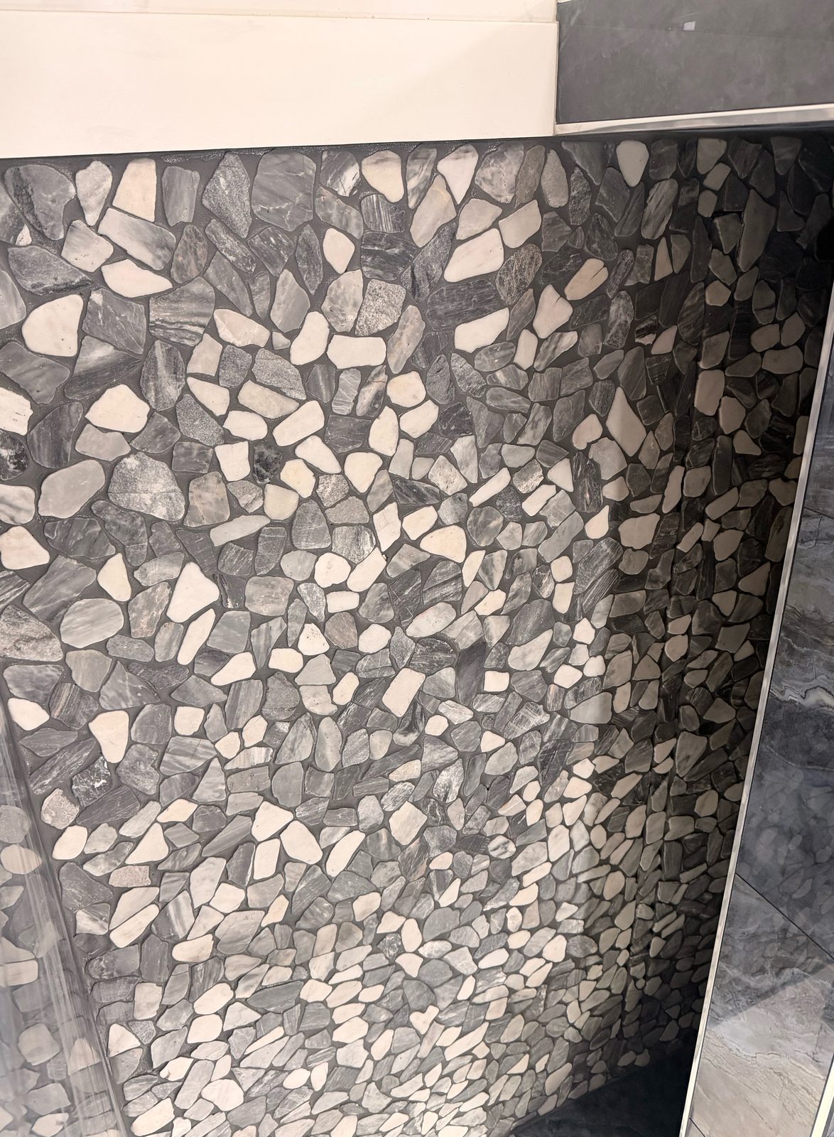 Pebble mosaic shower accent wall in gray and white stone with silver trim
