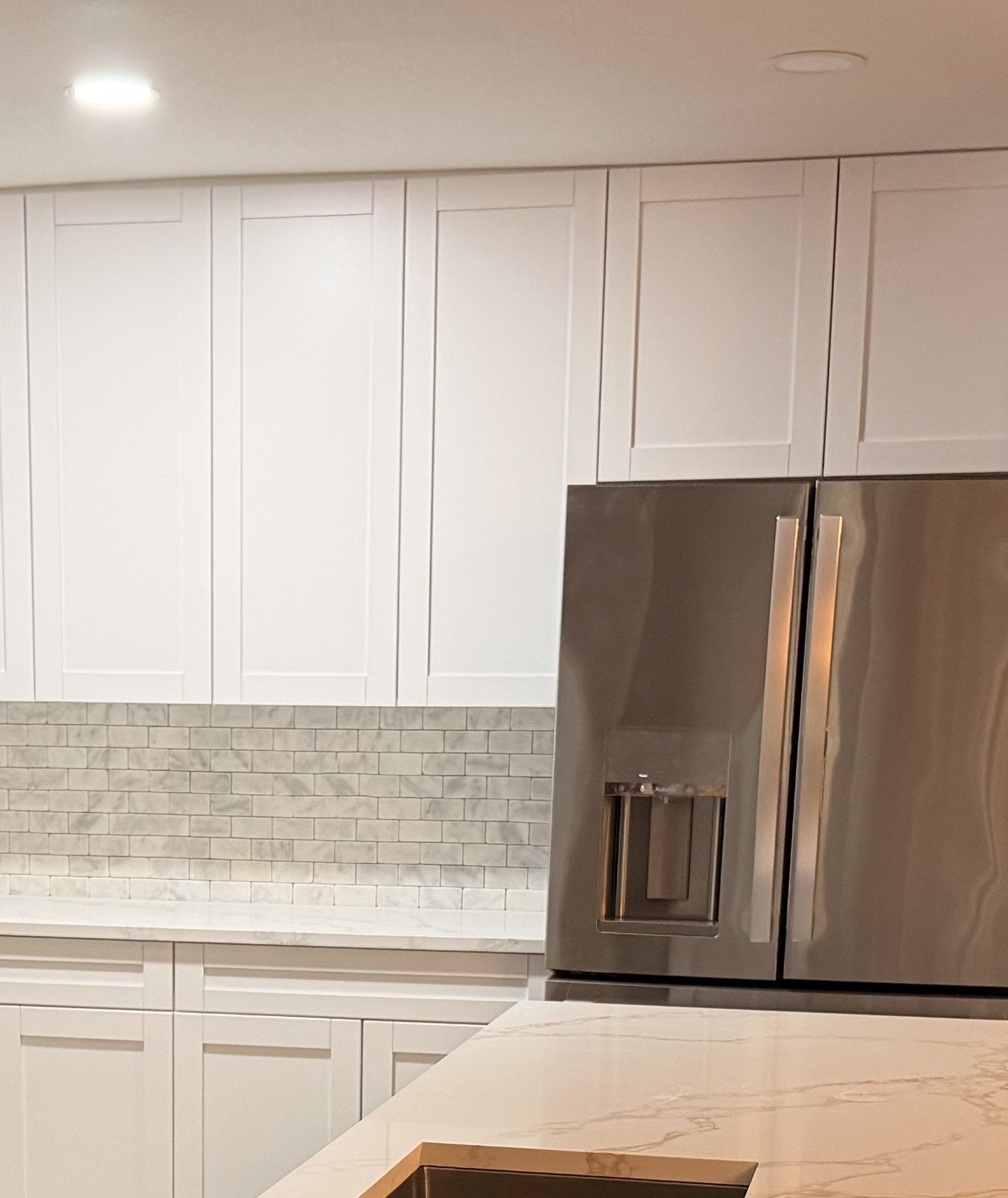 White shaker kitchen with marble-look counters, a center island, and a stainless French-door refrigerator